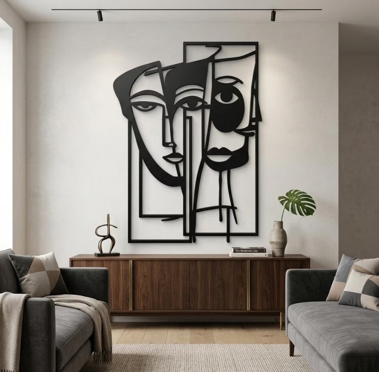 Escultura de pared Art by Amapola con diseño abstracto de rostros entrelazados en metal negro sobre pared blanca.